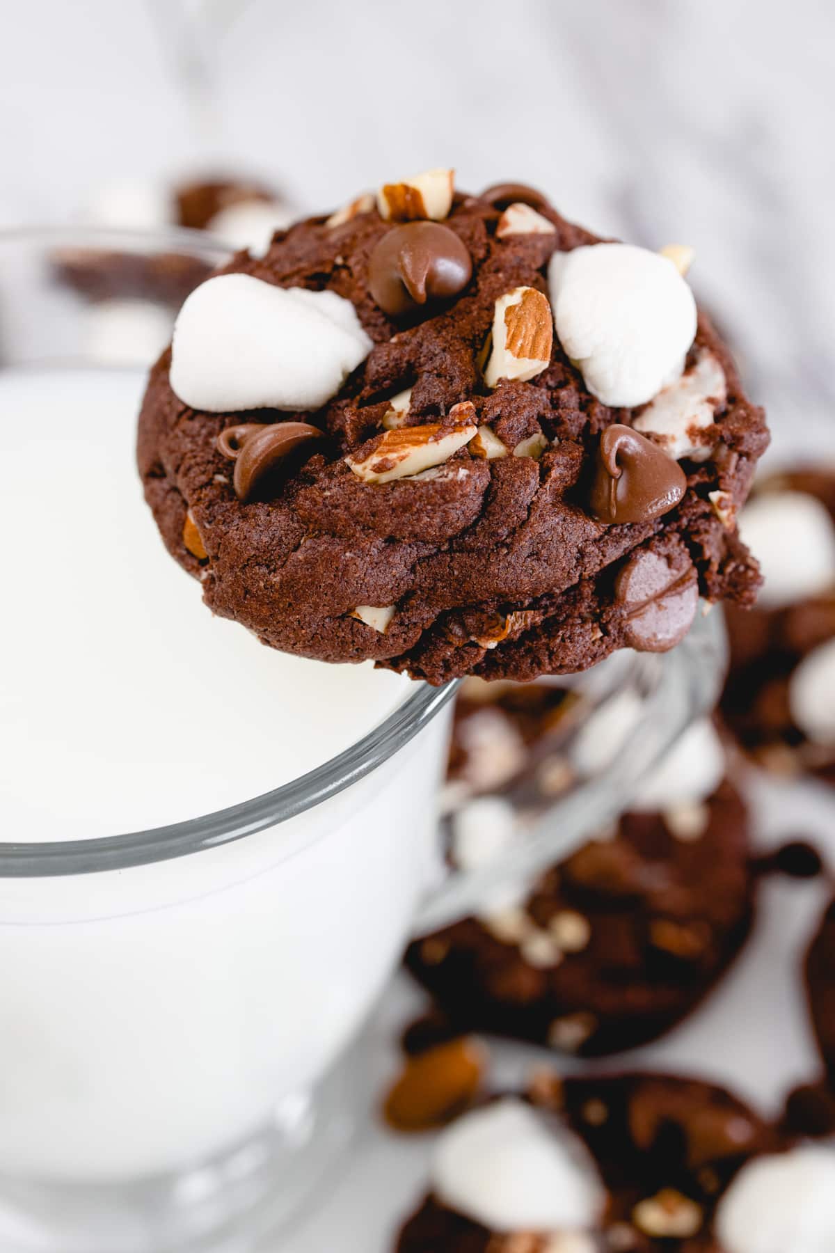 Close up of a rocky road cookie balanced on the side of a glass of milk.. 