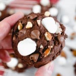 Close up of a chocolate rocky road cookie being held up in mid-air.