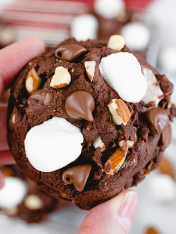 Close up of a chocolate rocky road cookie being held up in mid-air.
