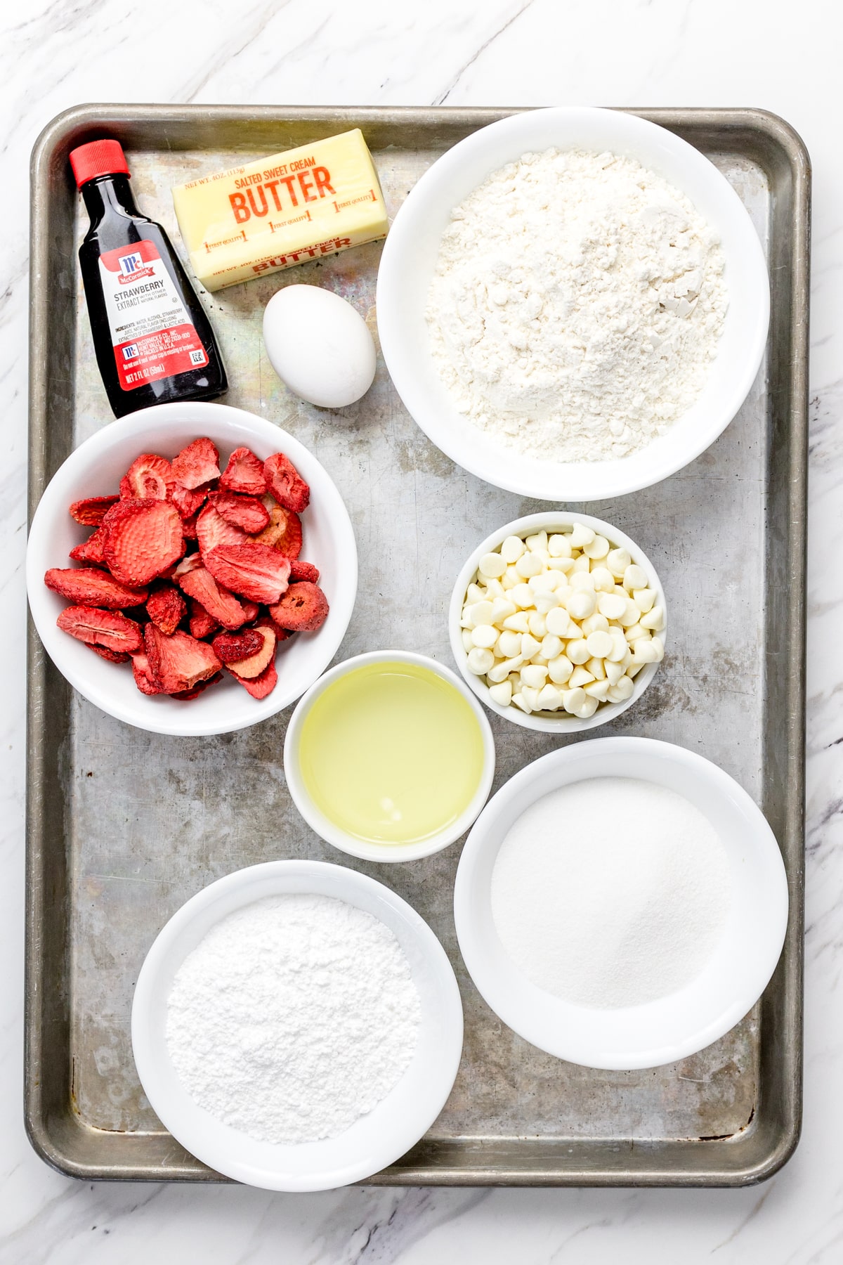 Top view of ingredients needed to make Strawberry white chocolate chip cookies in bowls on a baking tray.