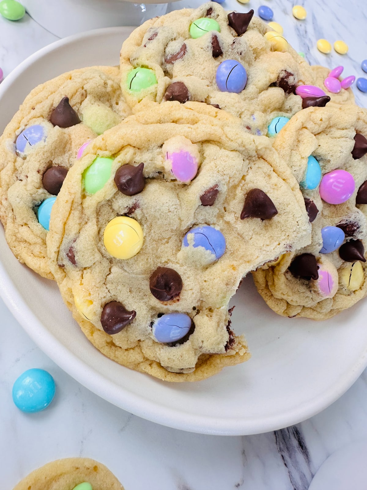 Close up of a plate filled with Easter M&M Cookies, and the cookie at the front has a bite taken out of it. 