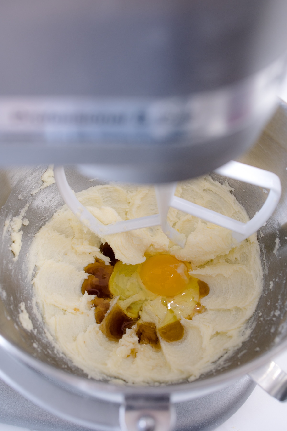 Close up of a stand mixer creaming a butter mixture with an egg and vanilla on top. 
