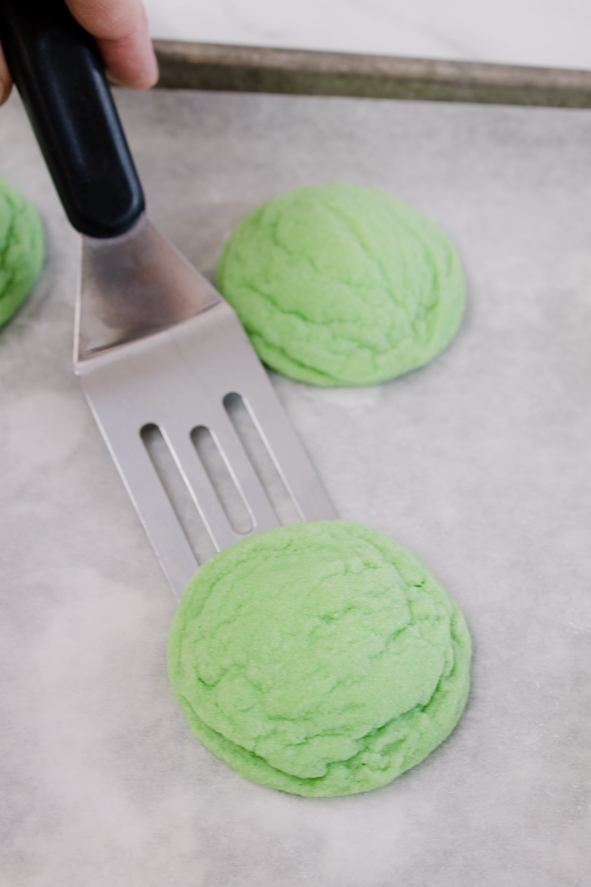 Close up of green cookies on a baking tray being scooped up by a spatula. 