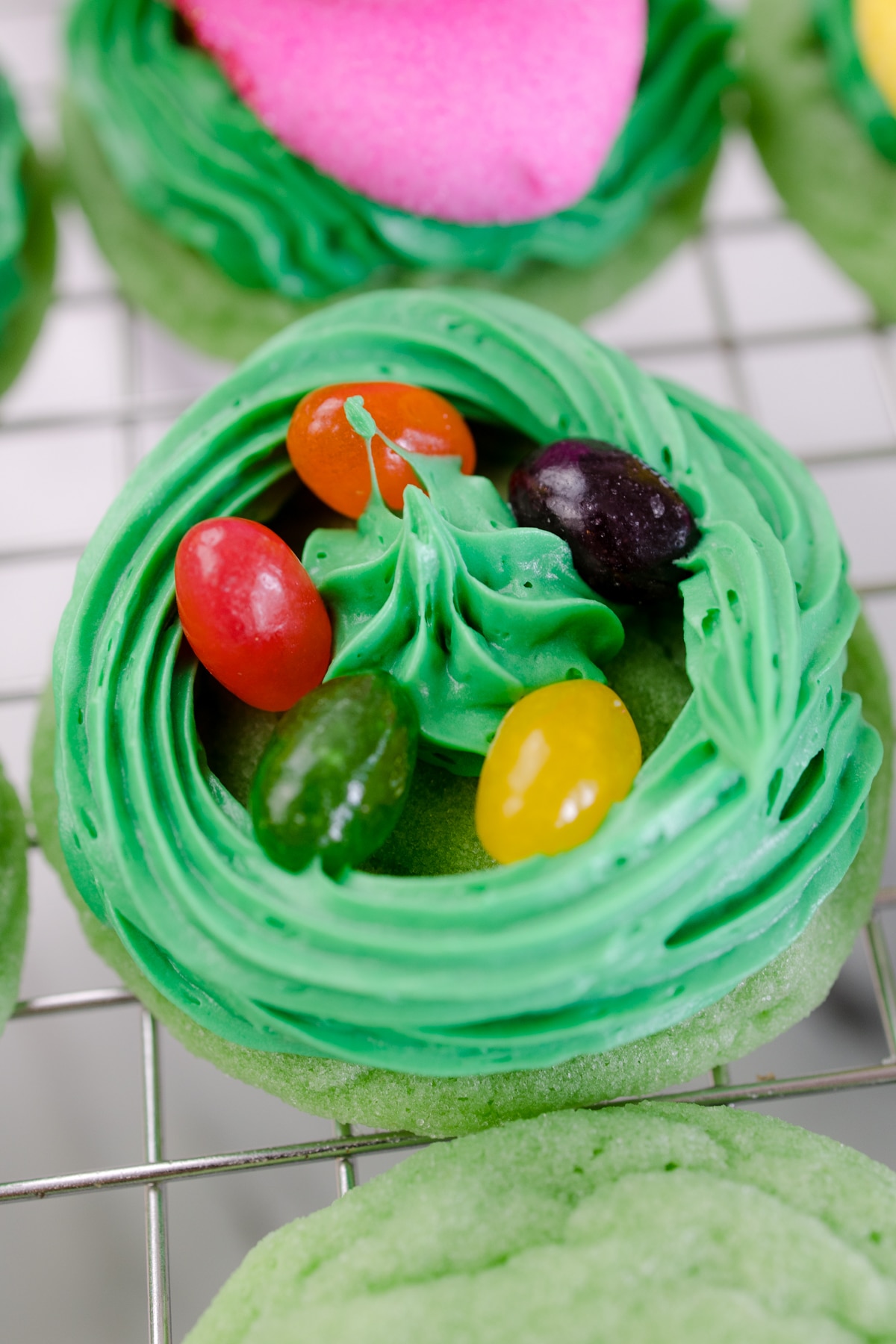 Close up of a green cookie with green frosting piped around the edge, filled with jelly beans, with a dollop of green frosting in the middle.