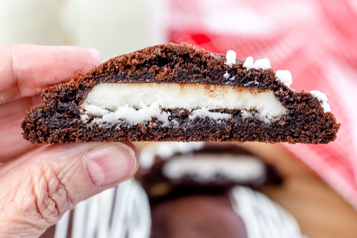 Close up of half a peppermint patty cookie being held in mid-air so you can see the peppermint patty inside. 
