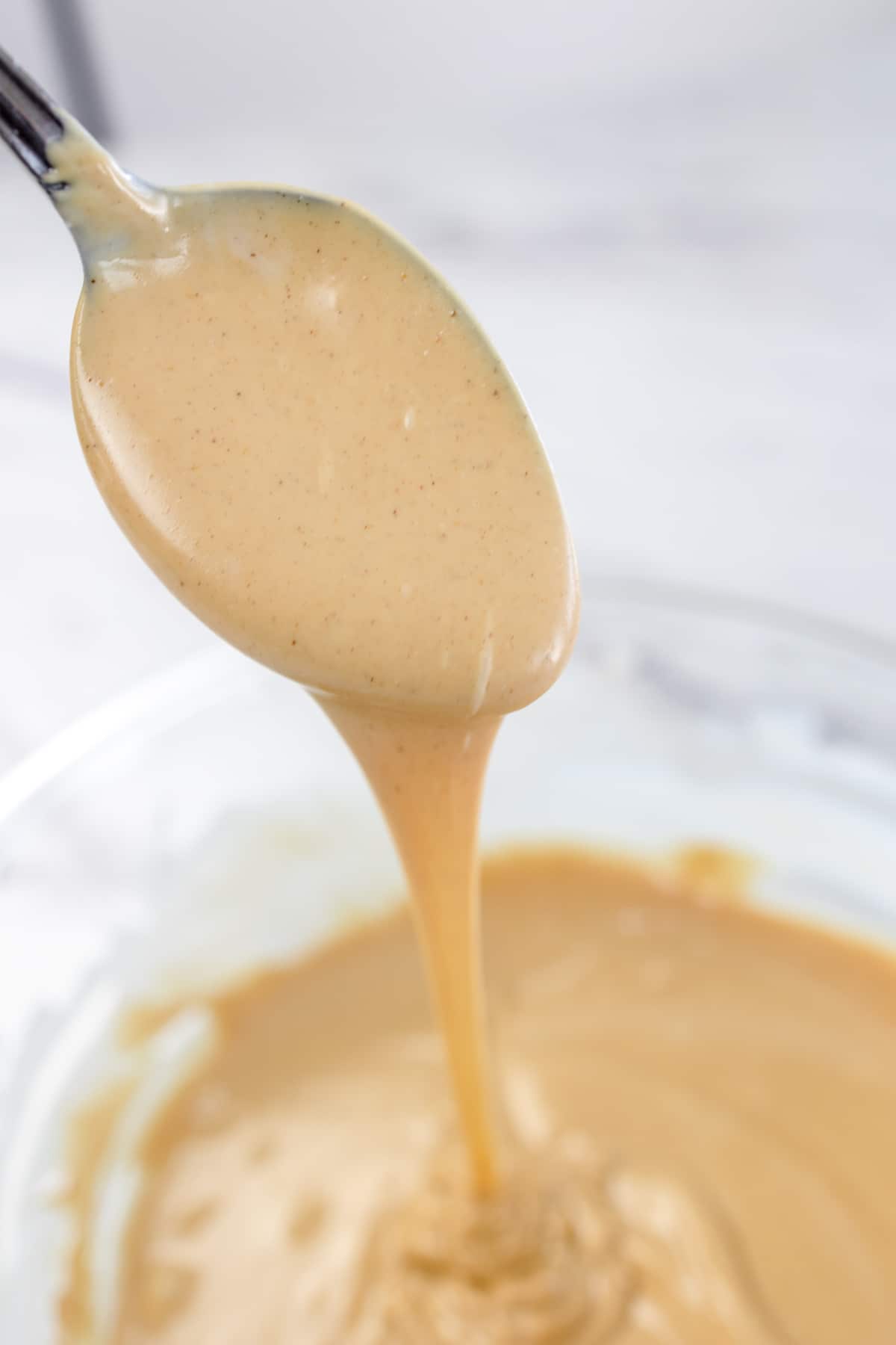 Close up of melted peanut butter and almond bark mixed together in a glass bowl, with a spoon lifting some out so that it is running off the spoon back into the bowl.