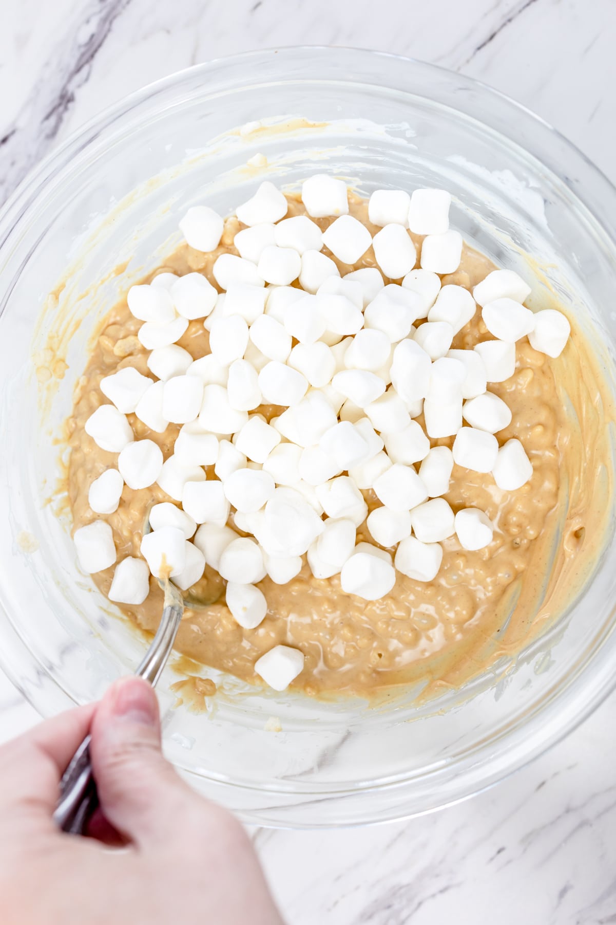 Top view of glass mixing bowl with Rice Krispie mixture in it and mini marshmallows on top.