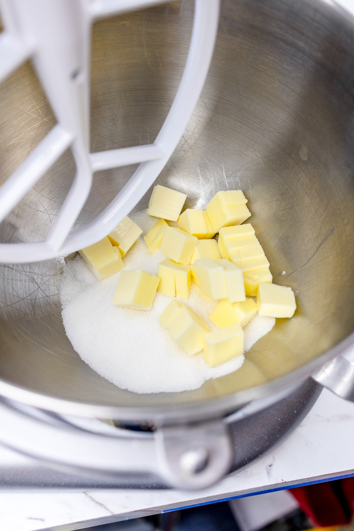 Close up of a mixing bowl with a paddle attachment with chopped butter and sugar in it.