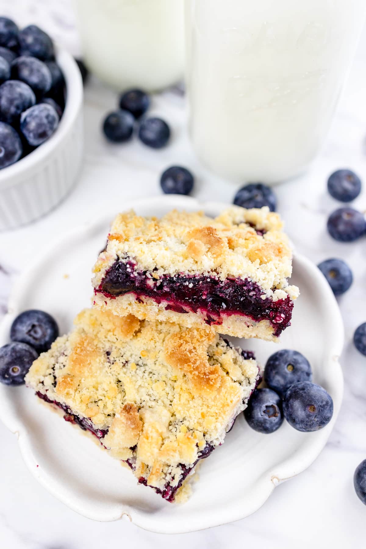 Two blueberry pie bars stacked on a white plate.