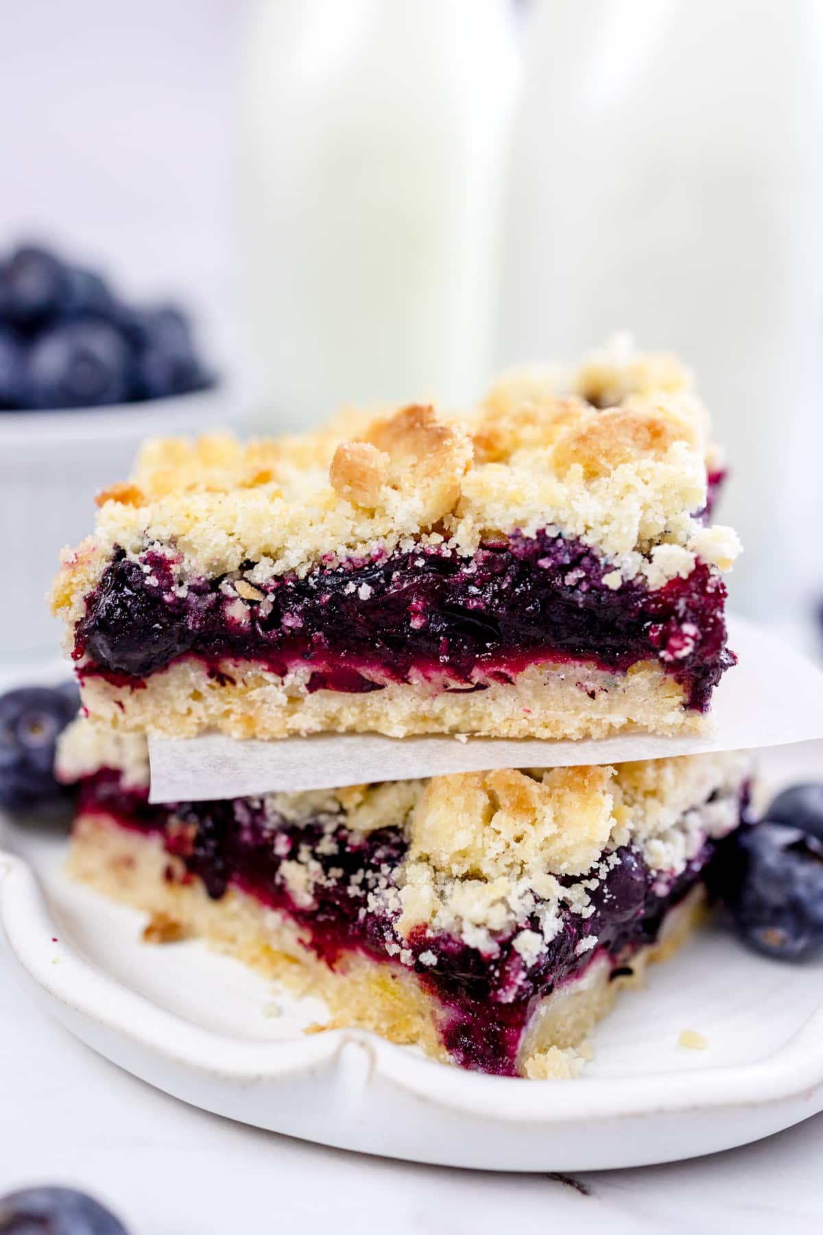 Close up of two blueberry pie bars stacked on a white plate.