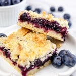 Close up of two blueberry pie bars stacked on a white plate.