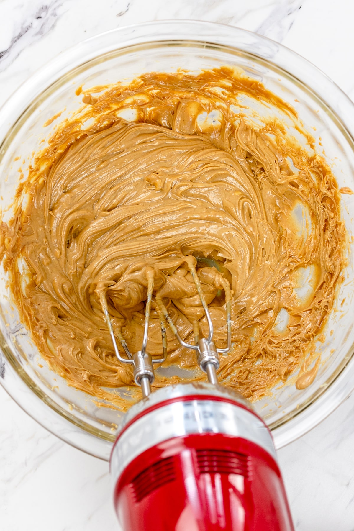 Top view of glass mixing bowl with peanut butter and butter being mixed together with a mixer.