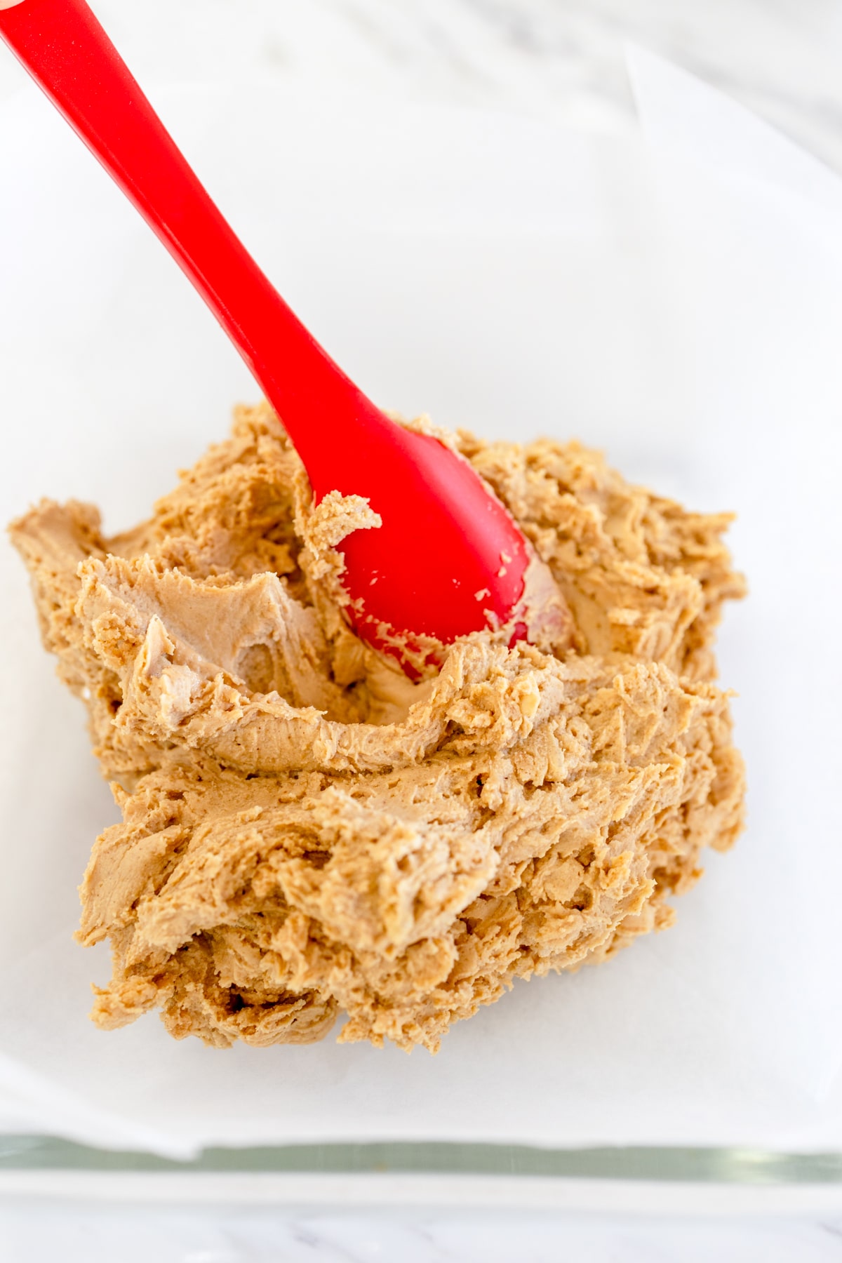 Close up of buckeye bar peanut butter mixture in the bottom of a baking dish with a spatula in it. 