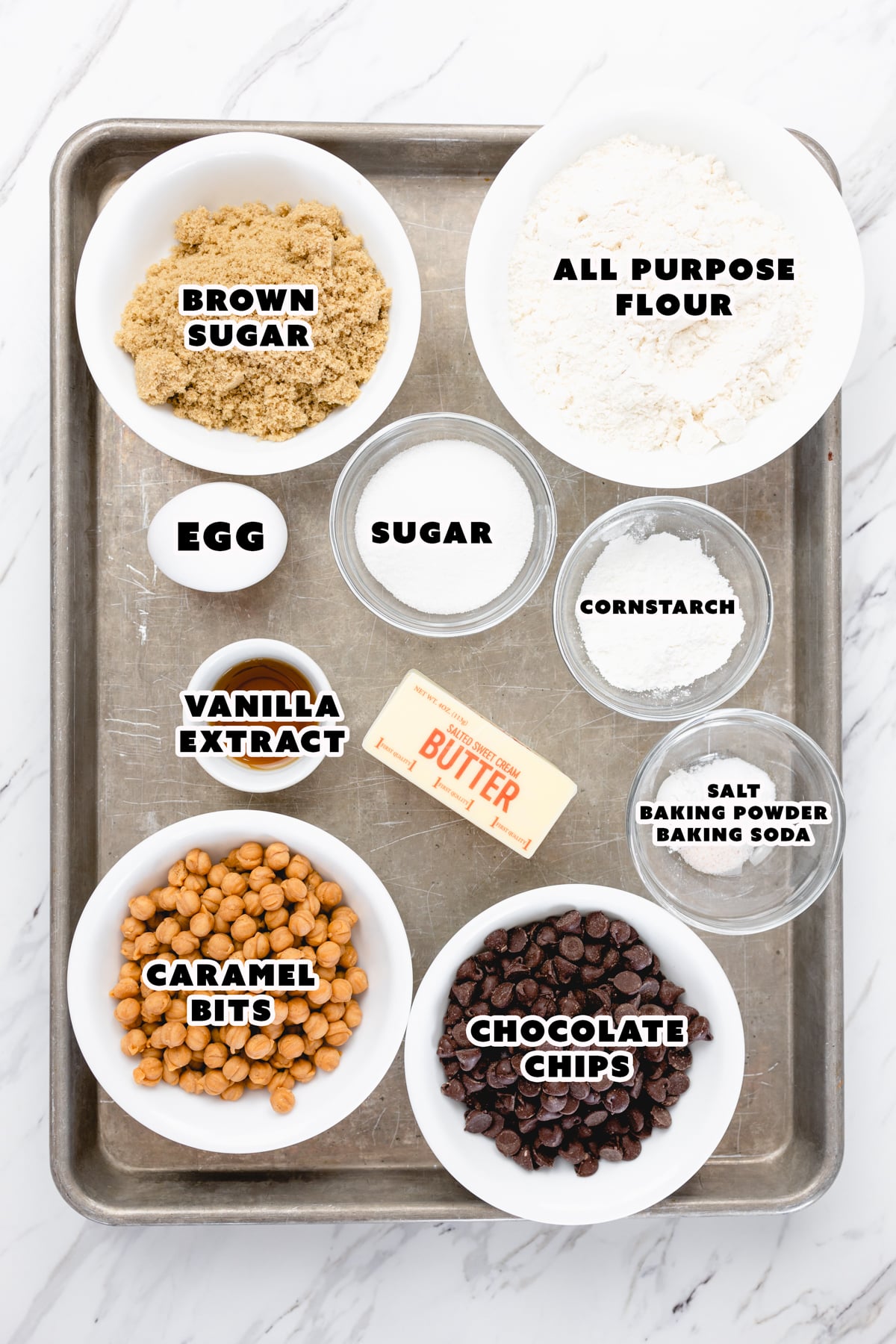 Top view of the ingredients needed to make caramel chocolate chip cookies in small bowls on a baking tray.