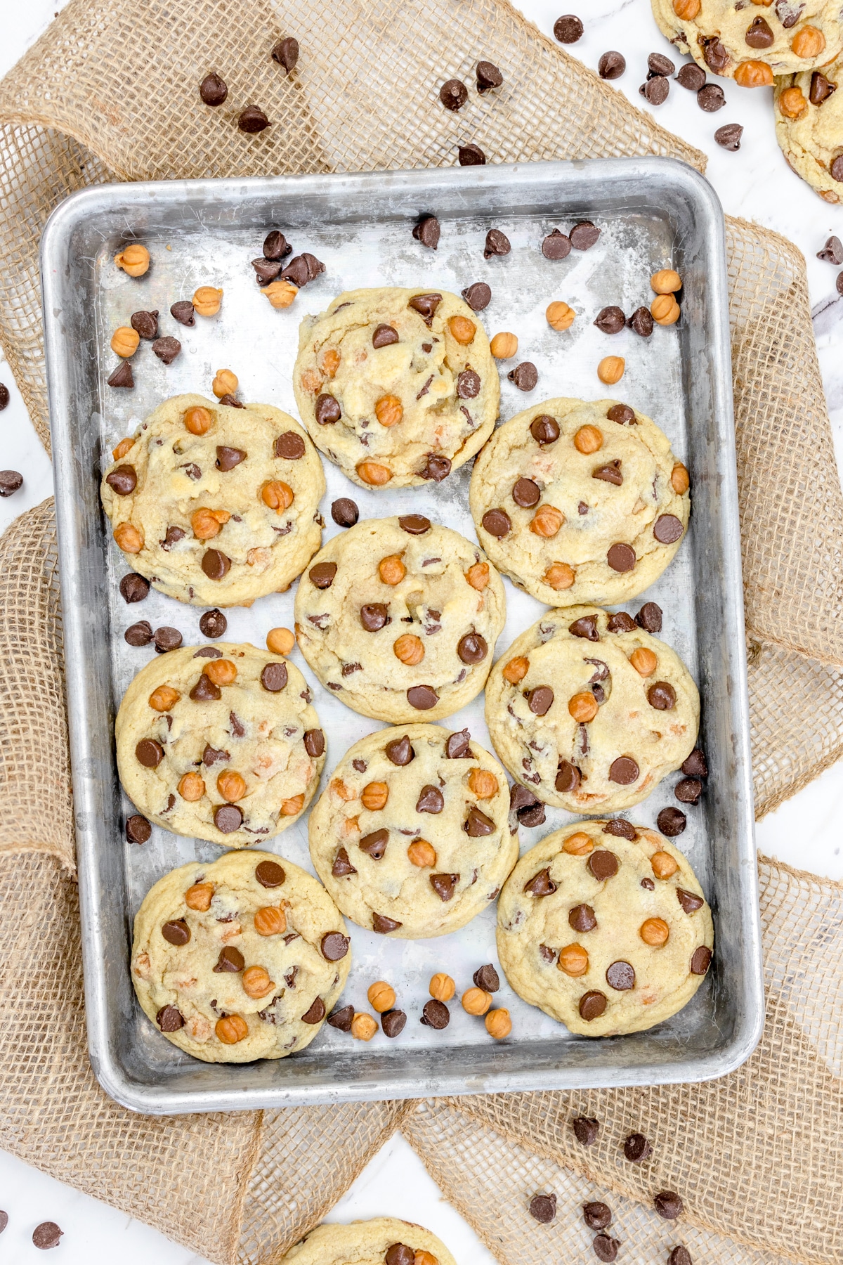 Top view of Caramel Chocolate Chip Cookies on a baking sheet with more chocoalte and caramel chips around them.