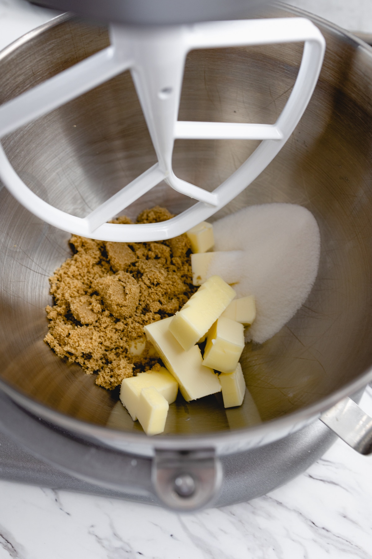 Close up of the bowl of a stand mixer with cubed butter, brown sugar, and white sugar in it.