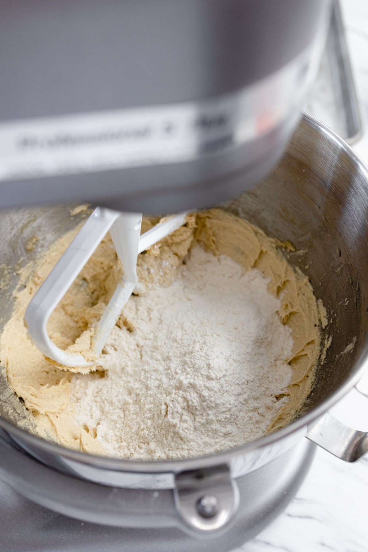 Close up of the bowl of a stand mixer with a creamed mixture in the bottom and a flour mioxture on top.