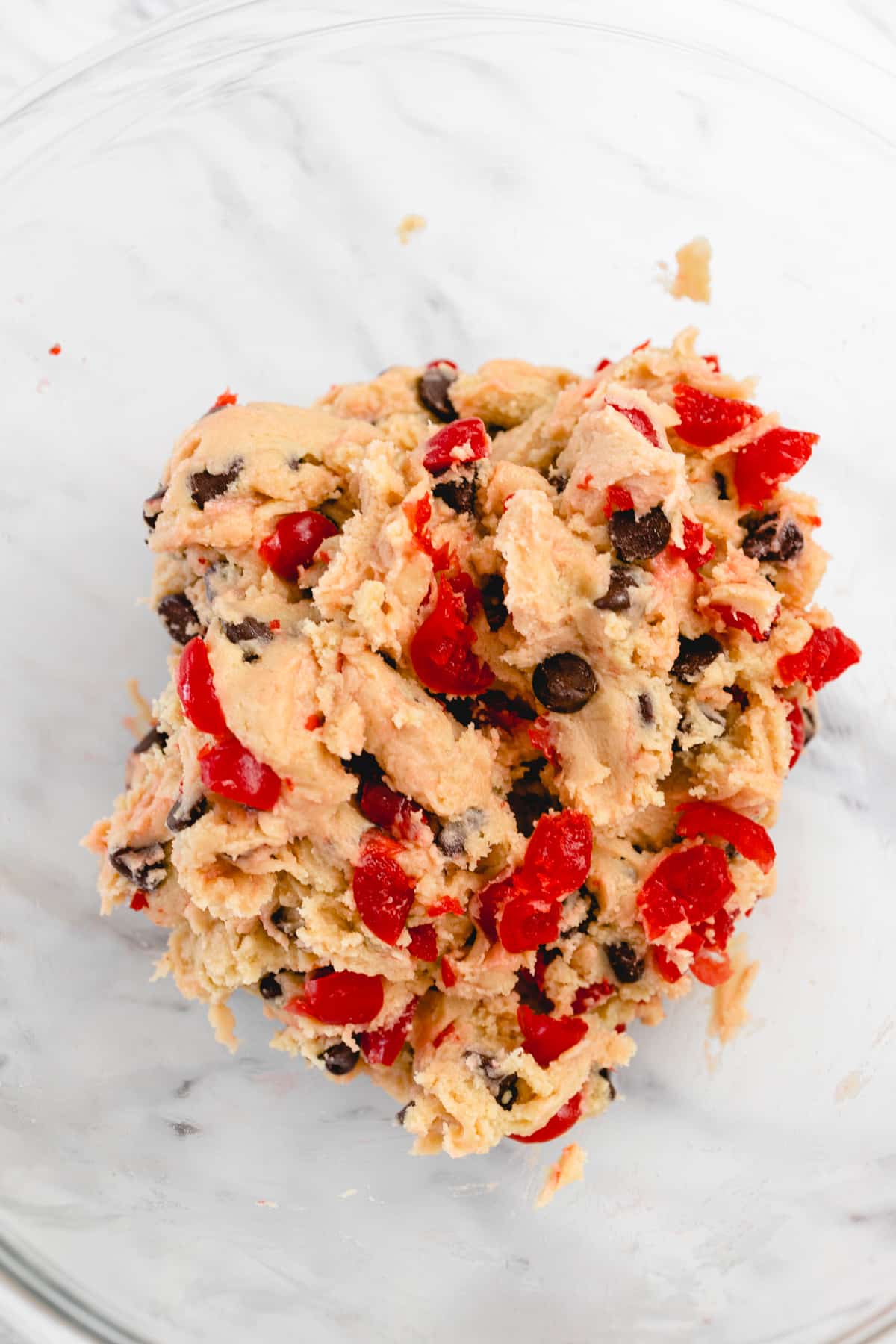 Top view close up of a glass mixing bowl with chocolate chip cherry cookie dough in it.