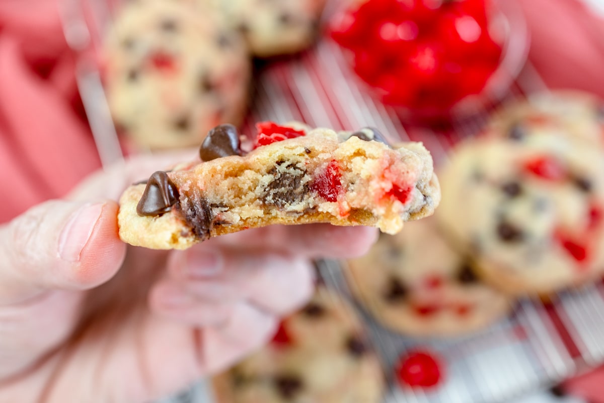 Close up of a halved Cherry Chocolate Chip Cookie being held in mid air by a hand.