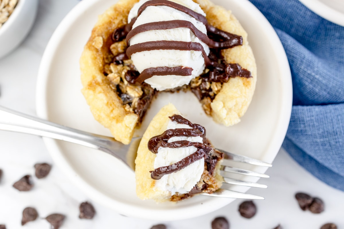 Top view of a chocolate chip pie cookie on a white plate with some of it on a fork lying on the side of the plate. 