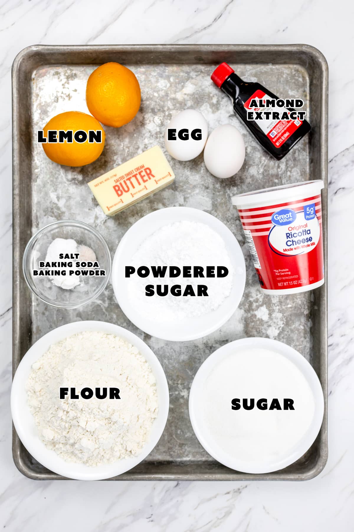 Top view of ingredients needed to make lemon ricotta cookies in small bowls on a baking tray.
