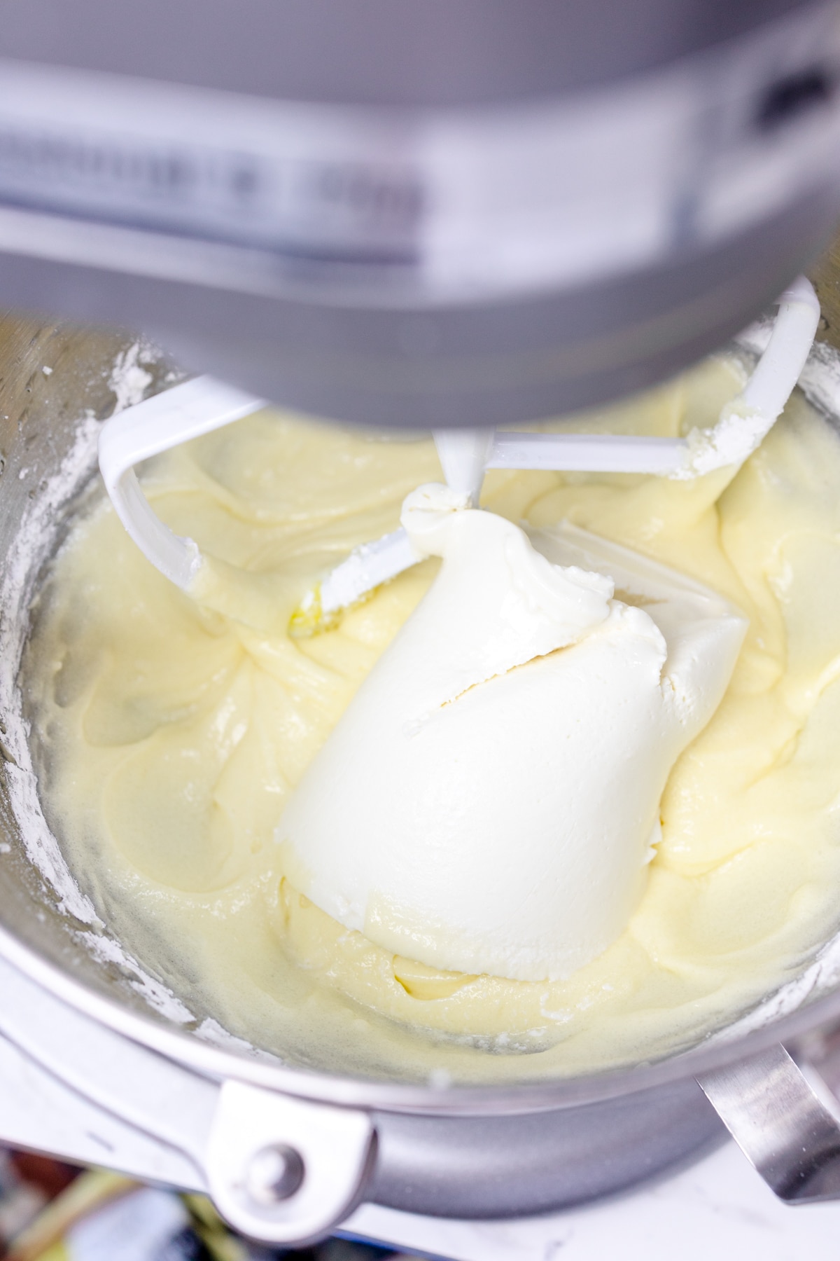 Close up of a stand mixer bowl with creamed butter and sugar in it with Ricotta Cheese on top.