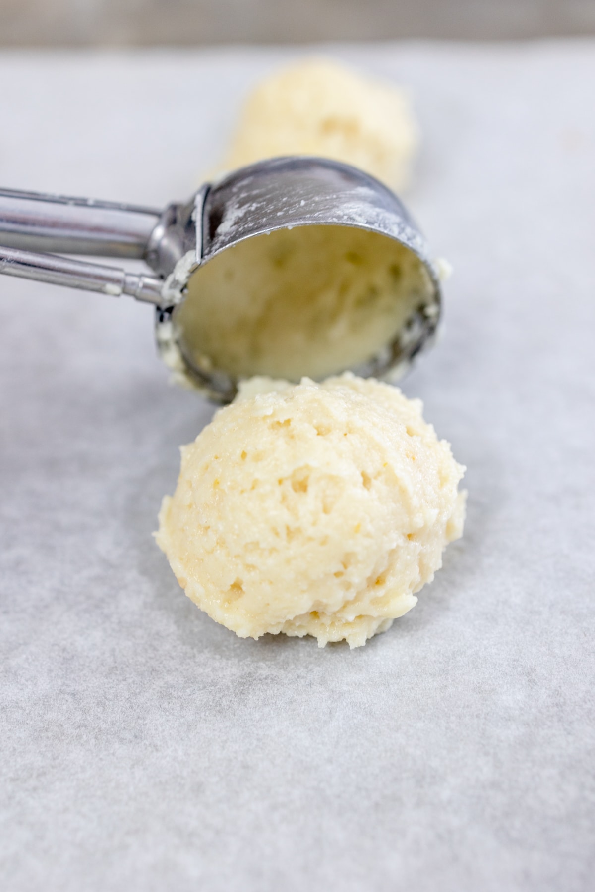 Close up of a cookie scoop putting a cookie dough ball onto a parchment paper lined tray.