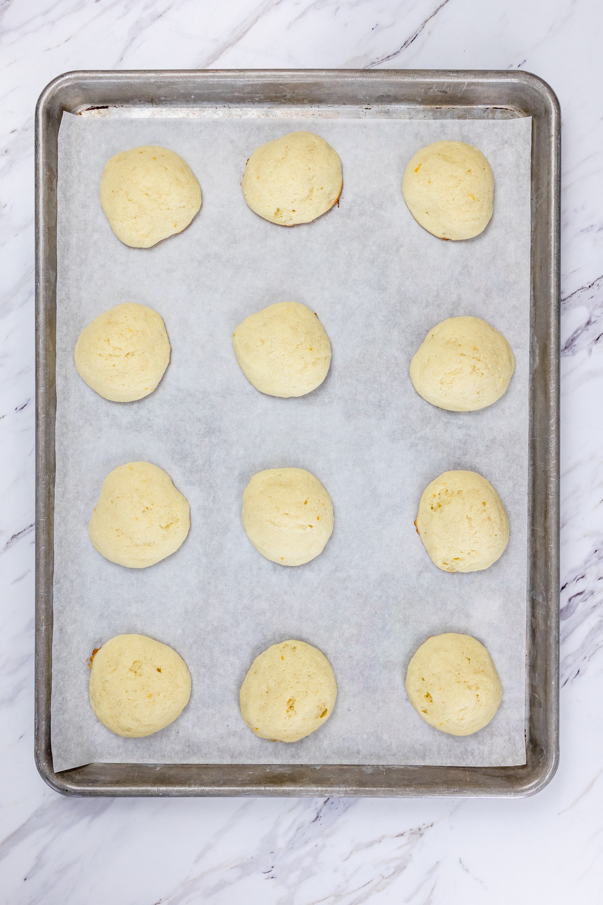 Top view of a baking tray with lemon ricotta cookie dough balls lined on it.