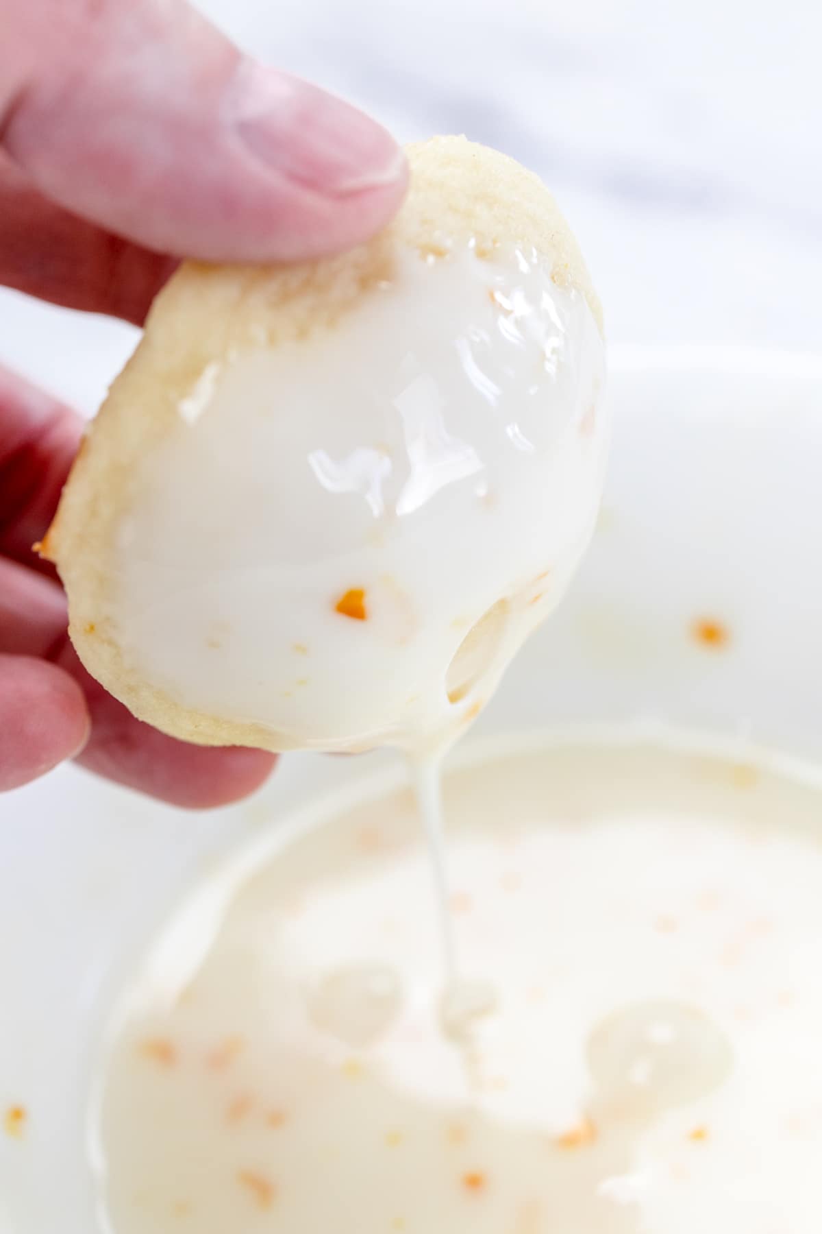 A Lemon ricotta cookie being held in mid air with frosting dripping off it.