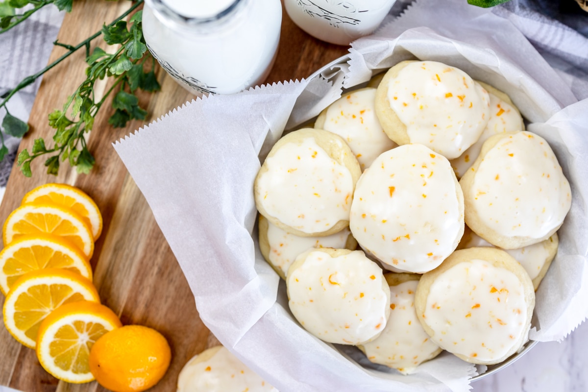 Top view of lemon ricotta cookies on parchment paper in a bowl next to a sliced orange.