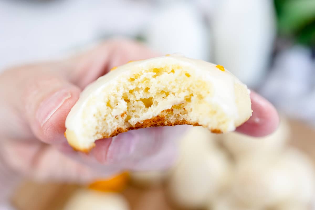Close up of a lemon ricotta cookie being helf in mid air by a hand with a bite taken out of it.