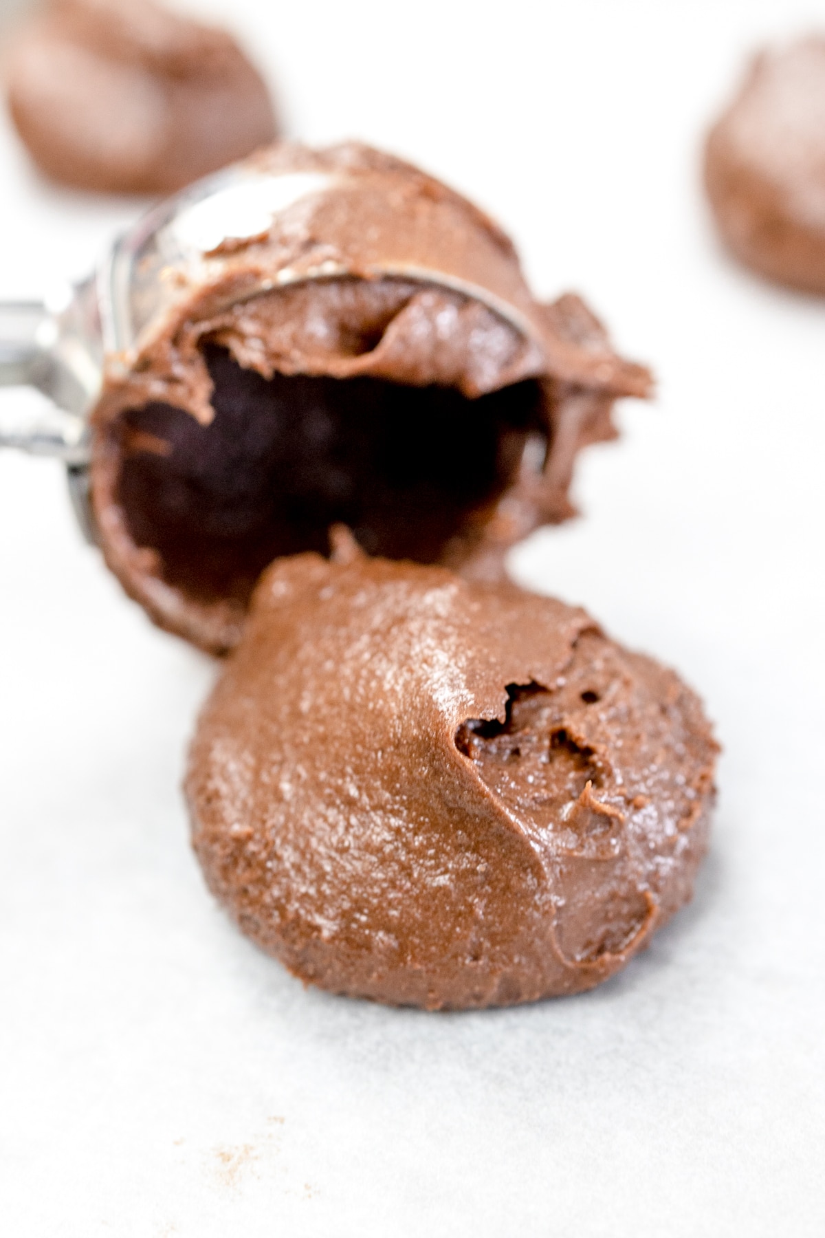 Close up of a texas sheet cake cookie dough ball being placed onto parchment paper with a cookie scoop. 