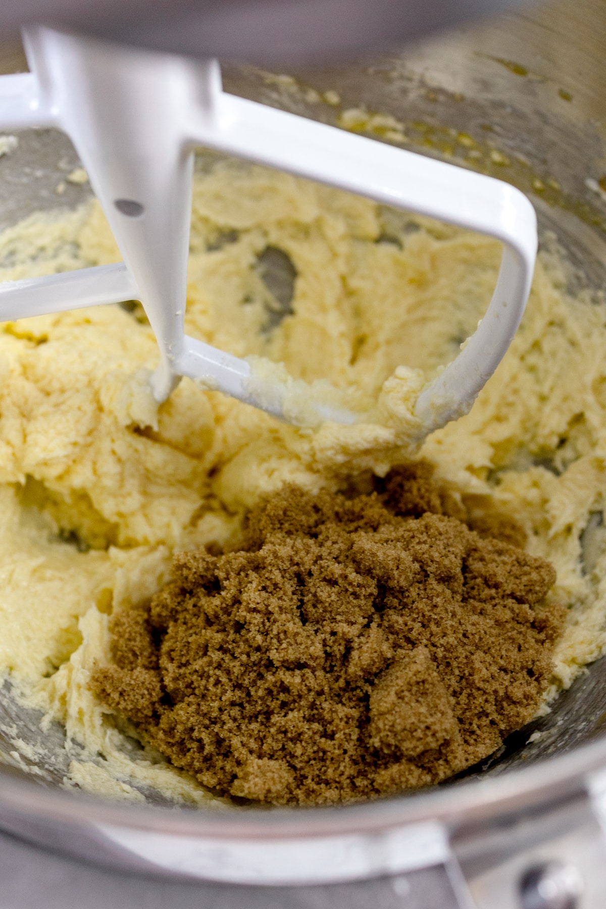 Close up of a bowl of a stand mixer with a butter and sugar mixture in it with brown sugar sitting on top.