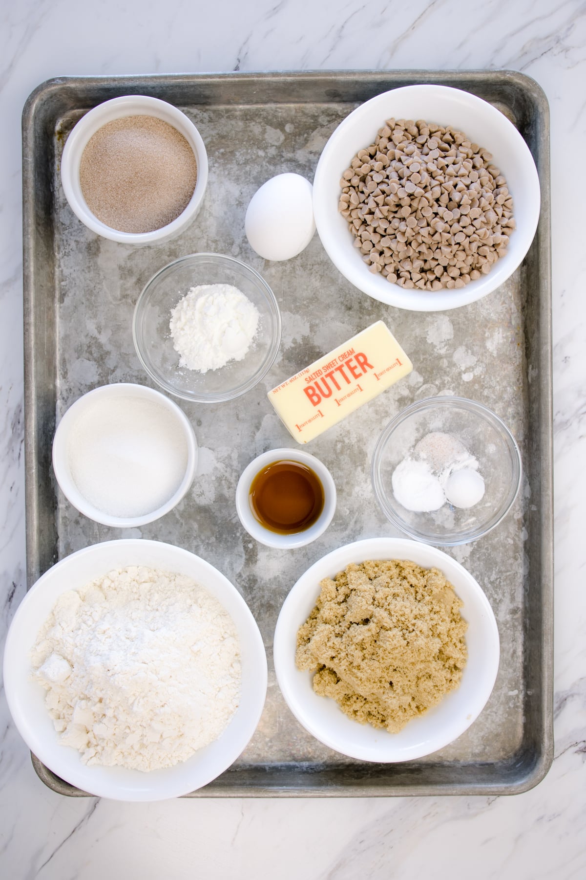 Top view of ingredients needed to make Cinnamon Chip Cookies in small bowls on a baking tray.