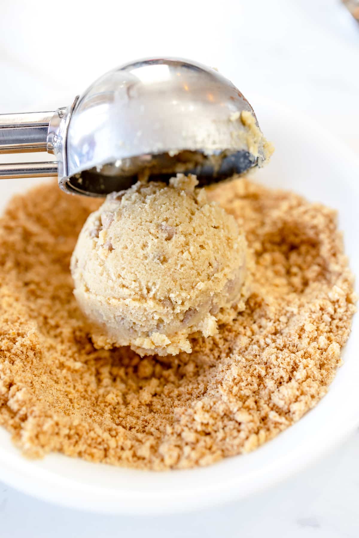 Close up of a cinnamon toast crunch cookie dough being scooped into a bowl of sugar.