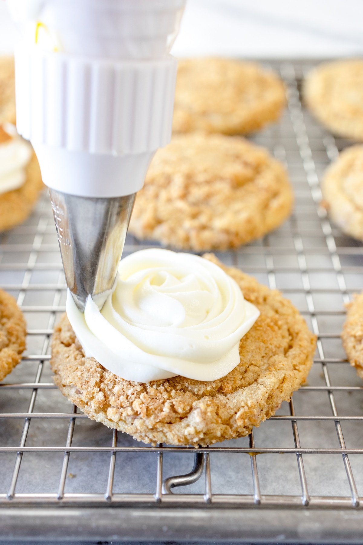 Close up of cinnamon toast crunch cookies on a wire rack being frosted with white frosting.