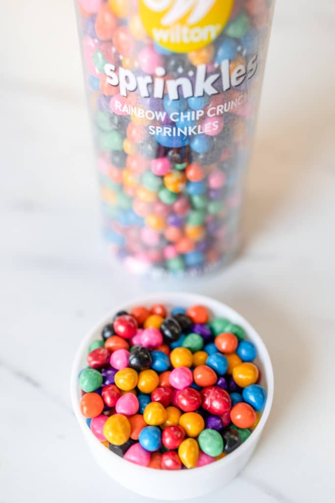 Close up of Wilton's rainbow colored sprinkles in a small bowl next to the tub..