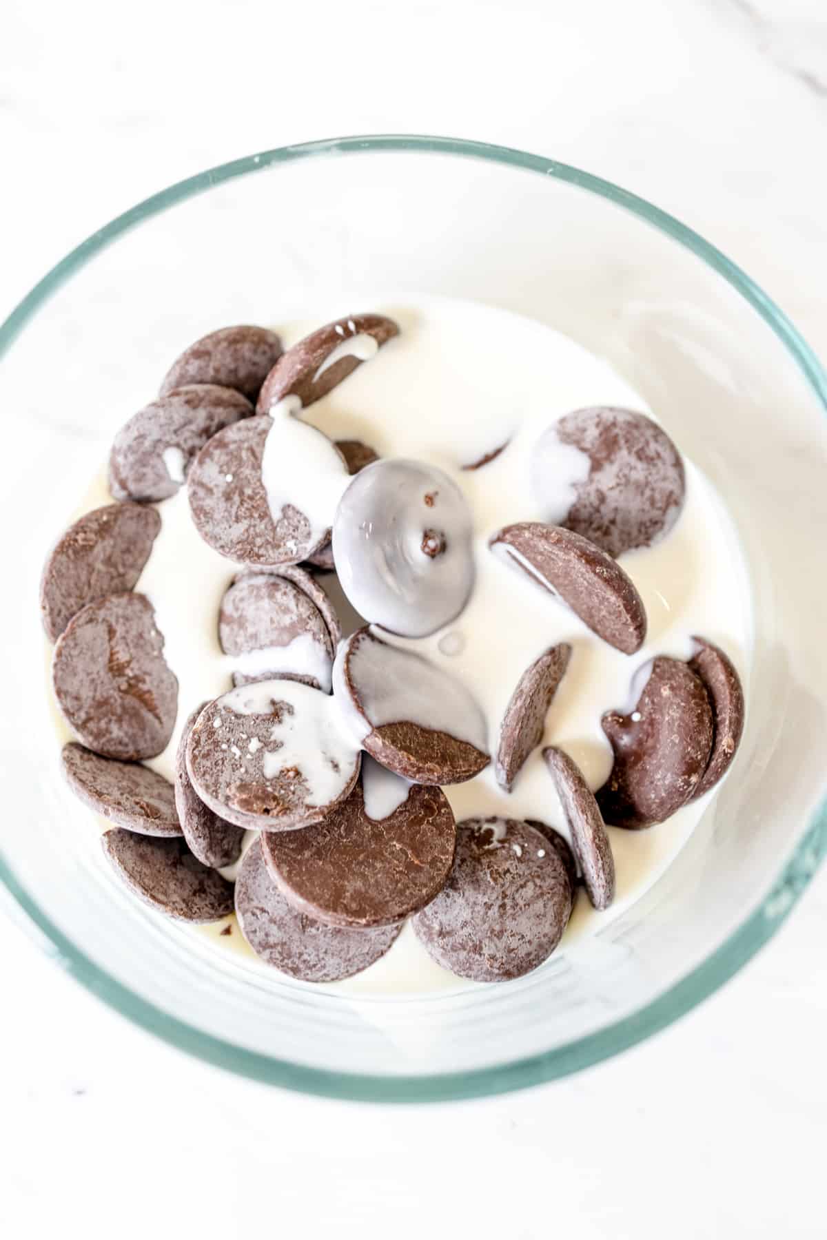 Top view of a glass mixing bowl with heavy cream and chocolate in it.