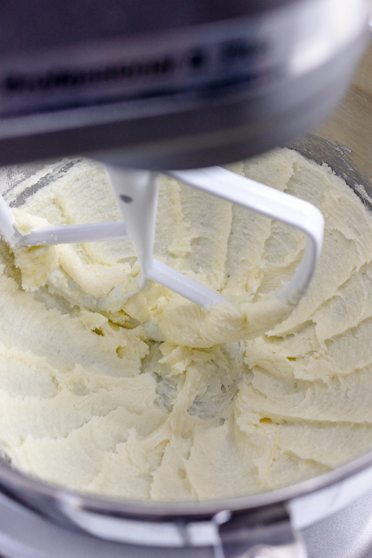 Close up of a bowl of a stand mixer with a paddle attachment with butter and sugar being creamed together.