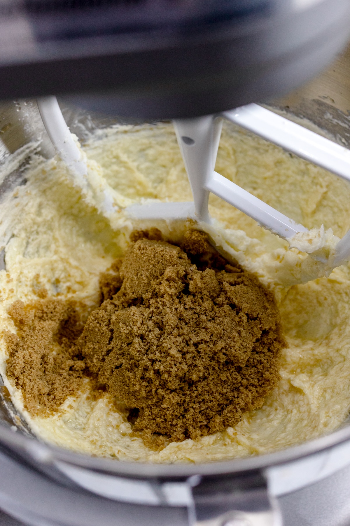 Close up of a bowl of a stand mixer with a paddle attachment with a creamed mixture in it and brown sugar on top.