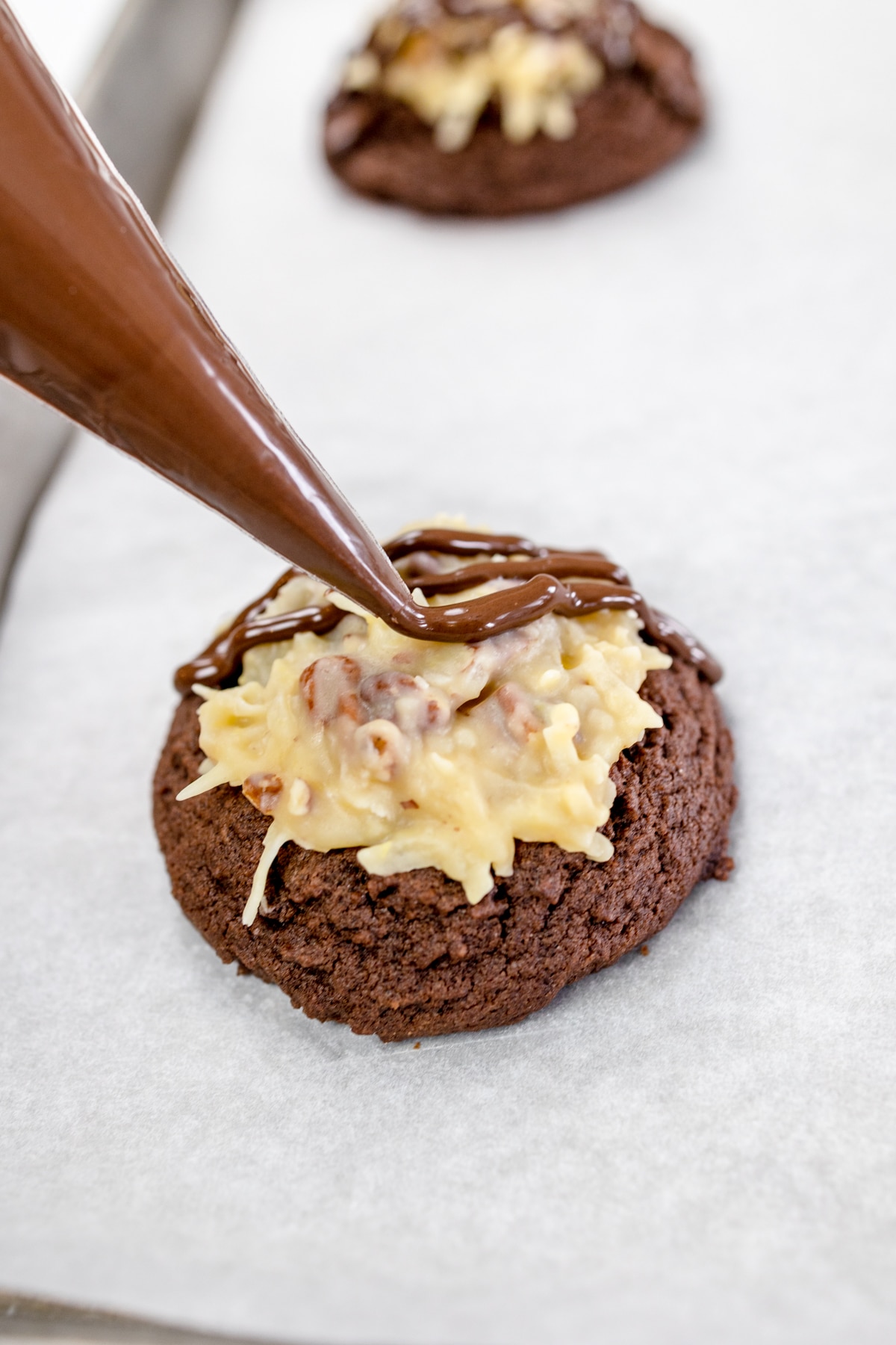 Close up of a German Chocolate Cake cookie with melted chocolate being drizzled on top with a frosting bag.