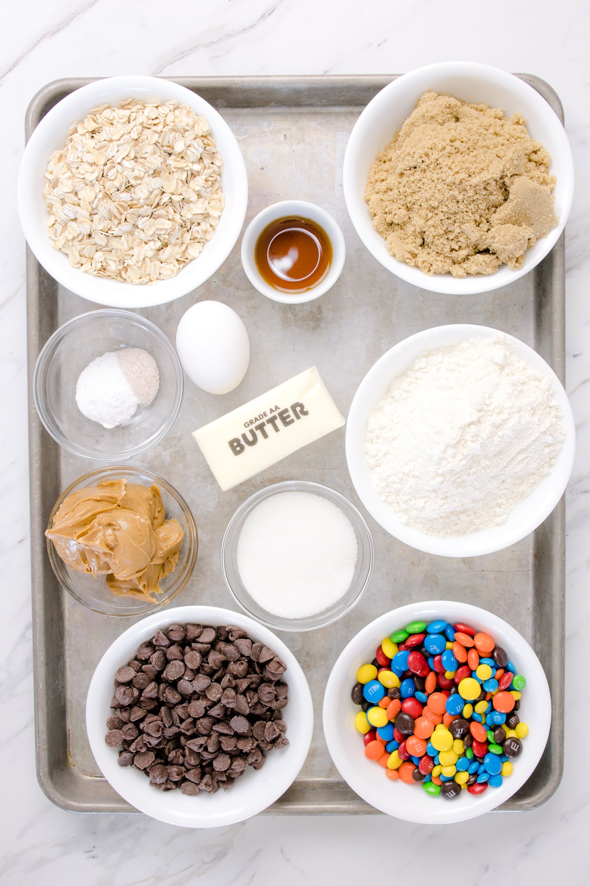 Top view of ingredients needed to mak emonster cookie bars in small boiwls on a baking sheet.