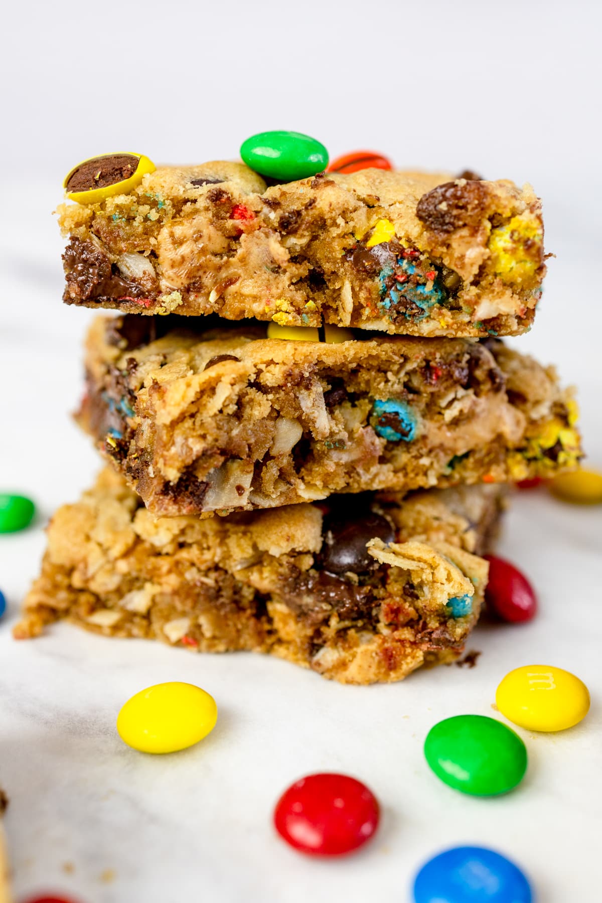 A stack of three Monster Cookie Bars on a white surface surrounded by M&Ms.