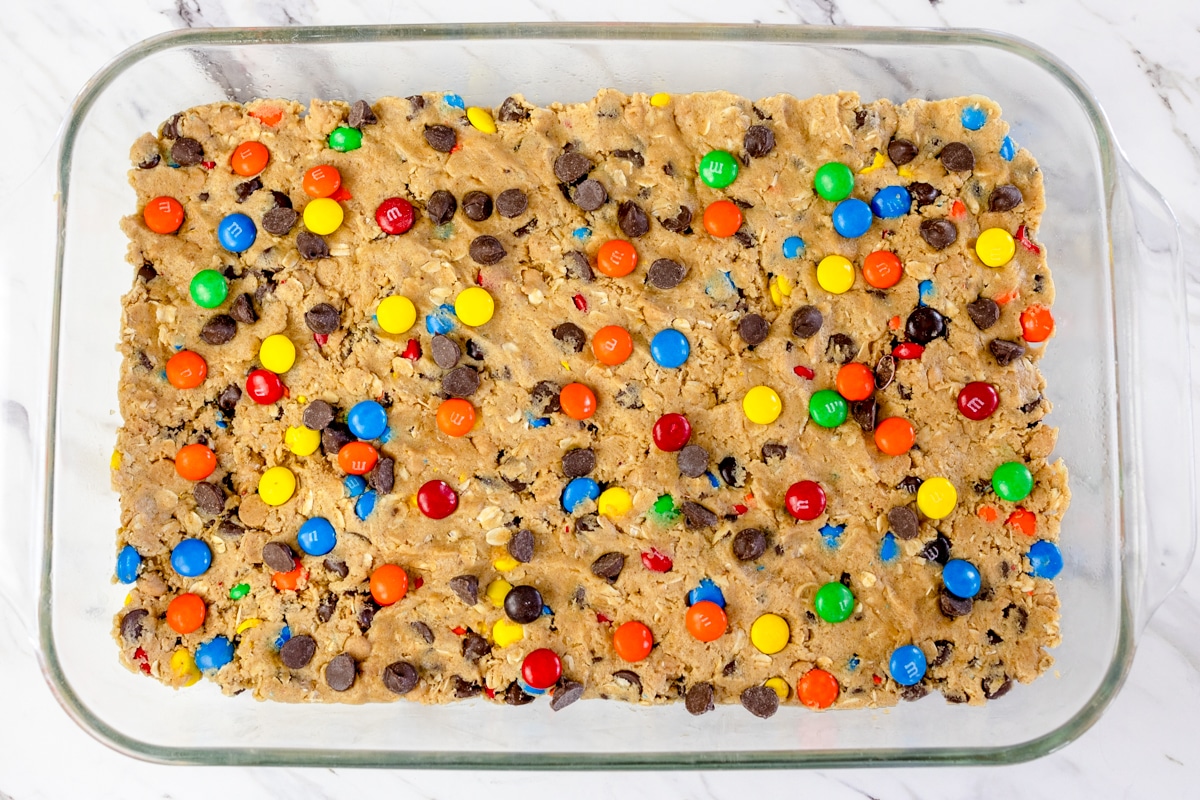 Top view of a glass baking dish with monster cookie bars cookie dough pressed into the bottom of it with extra M&Ms on top.