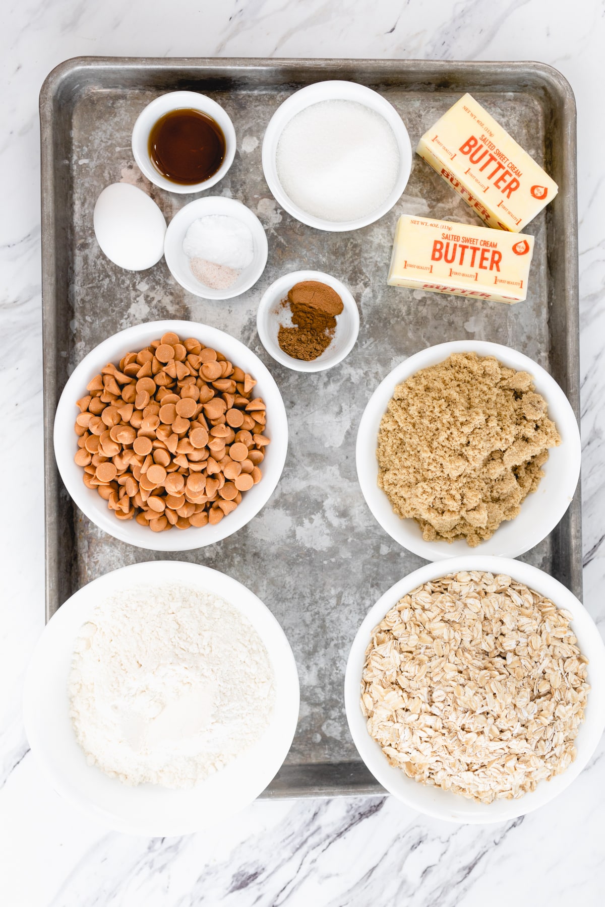 Top view of ingredients needed to make Oatmeal Butterscotch Cookies in small bowls on a baking tray.