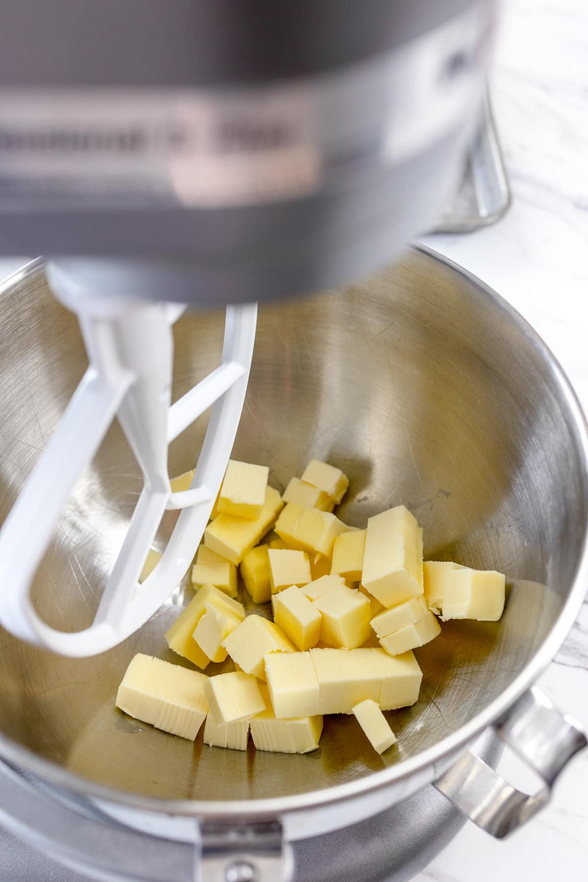 Close up of a bowl of a stand mixer with a paddle attachment about to cream cubes of butter.
