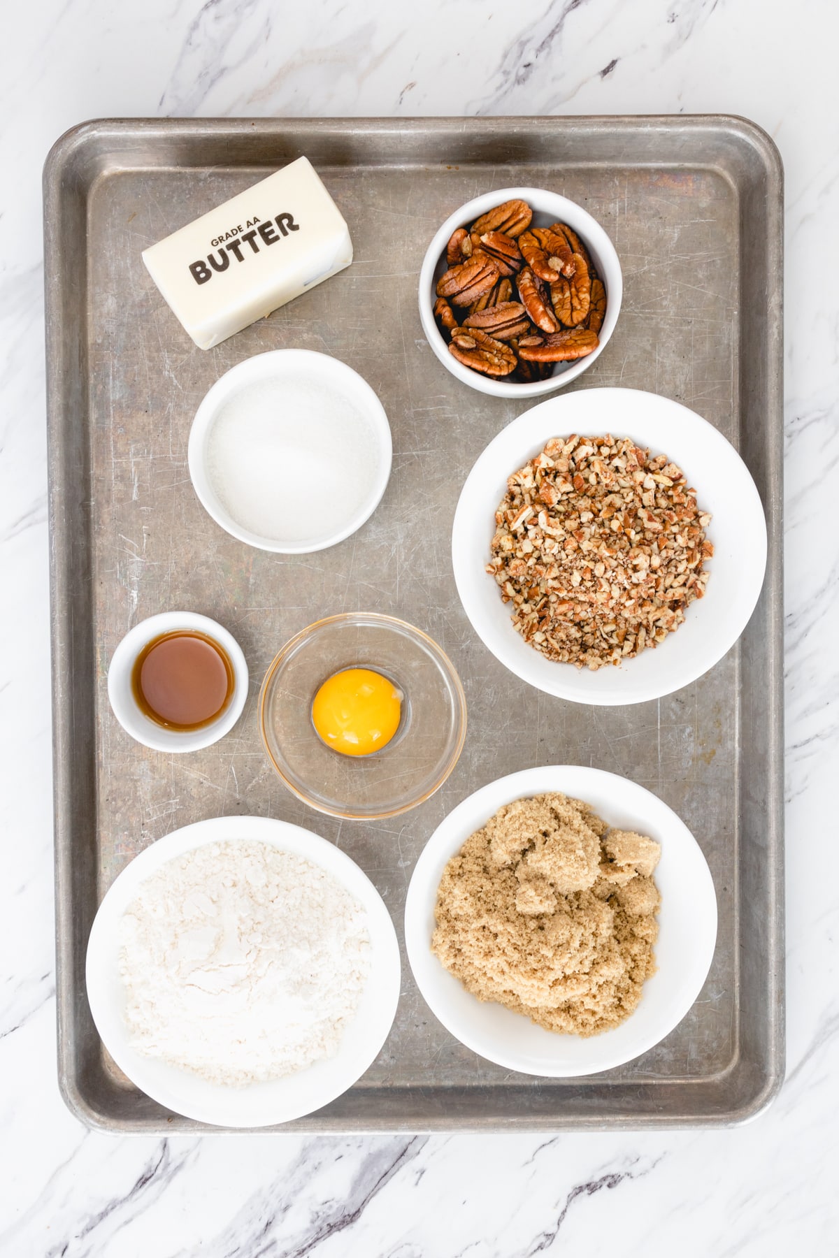 Top view of the ingredients needed for pecan sandies cookies in small bowls on a baking tray.
