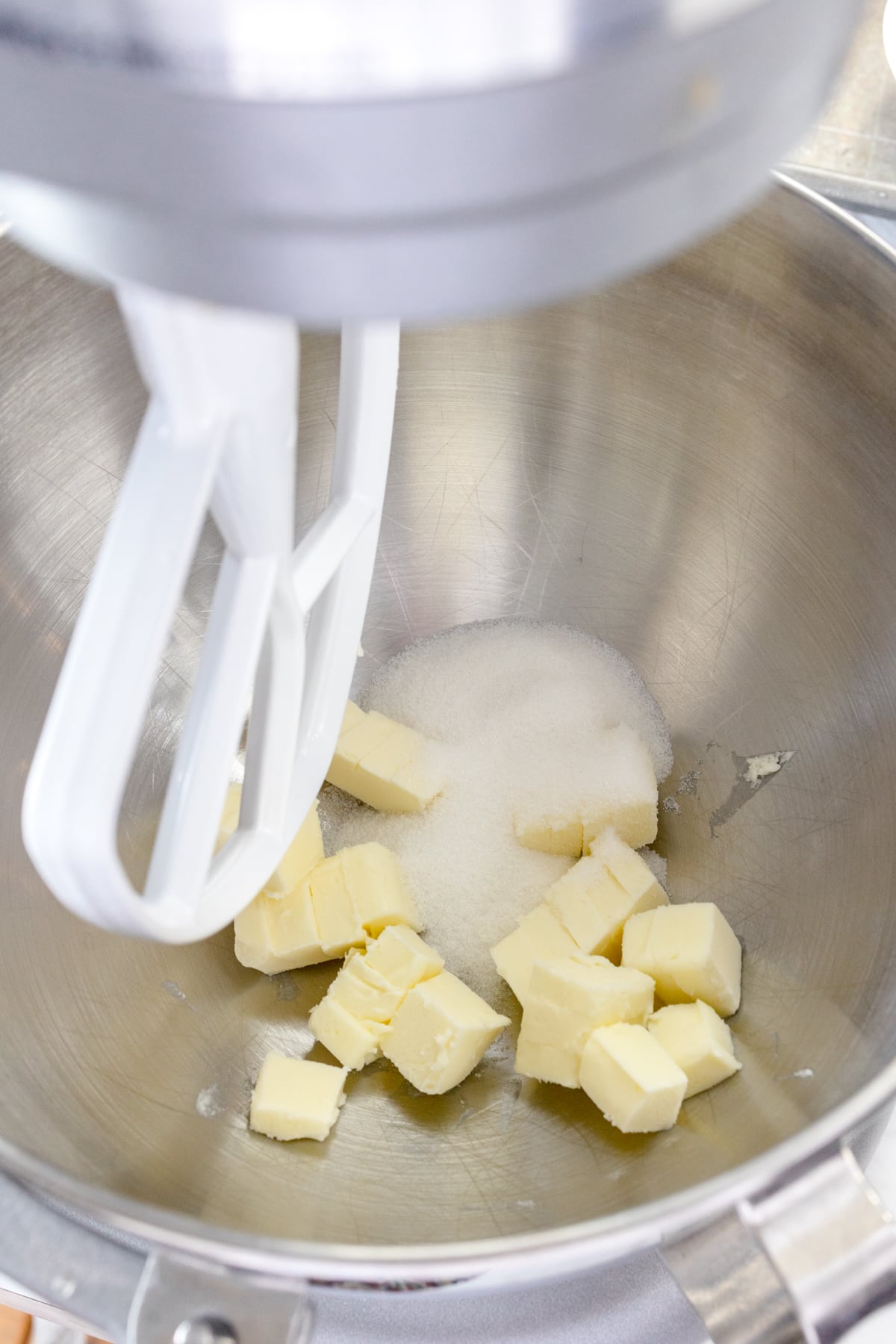Close up of the bowl of a stand mixeer with a paddle attachment with cubed butter and sugar in it.