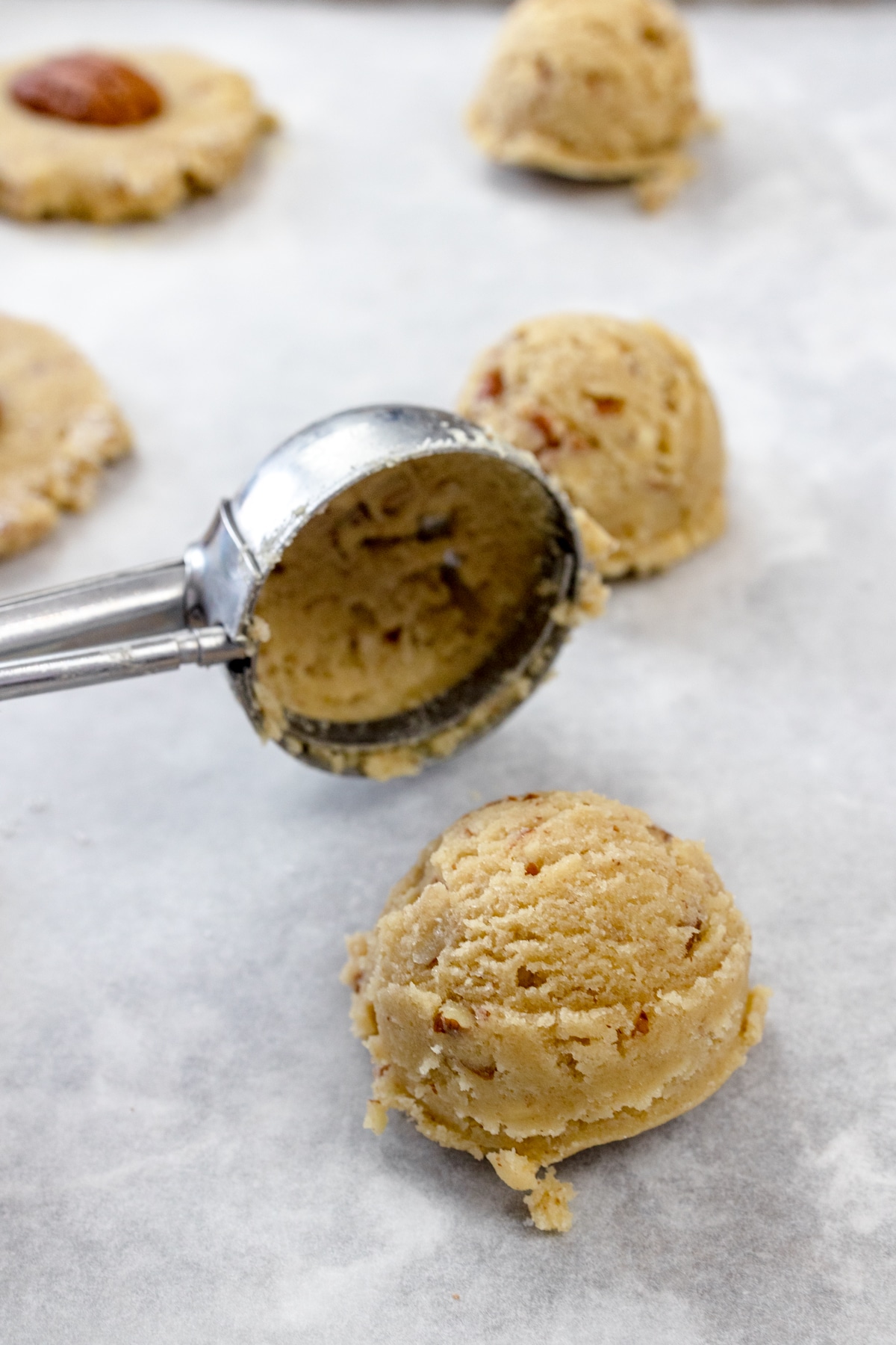 Close up of a cookie scoop hovering above a cookie dough ball on parchment paper on a baking tray.