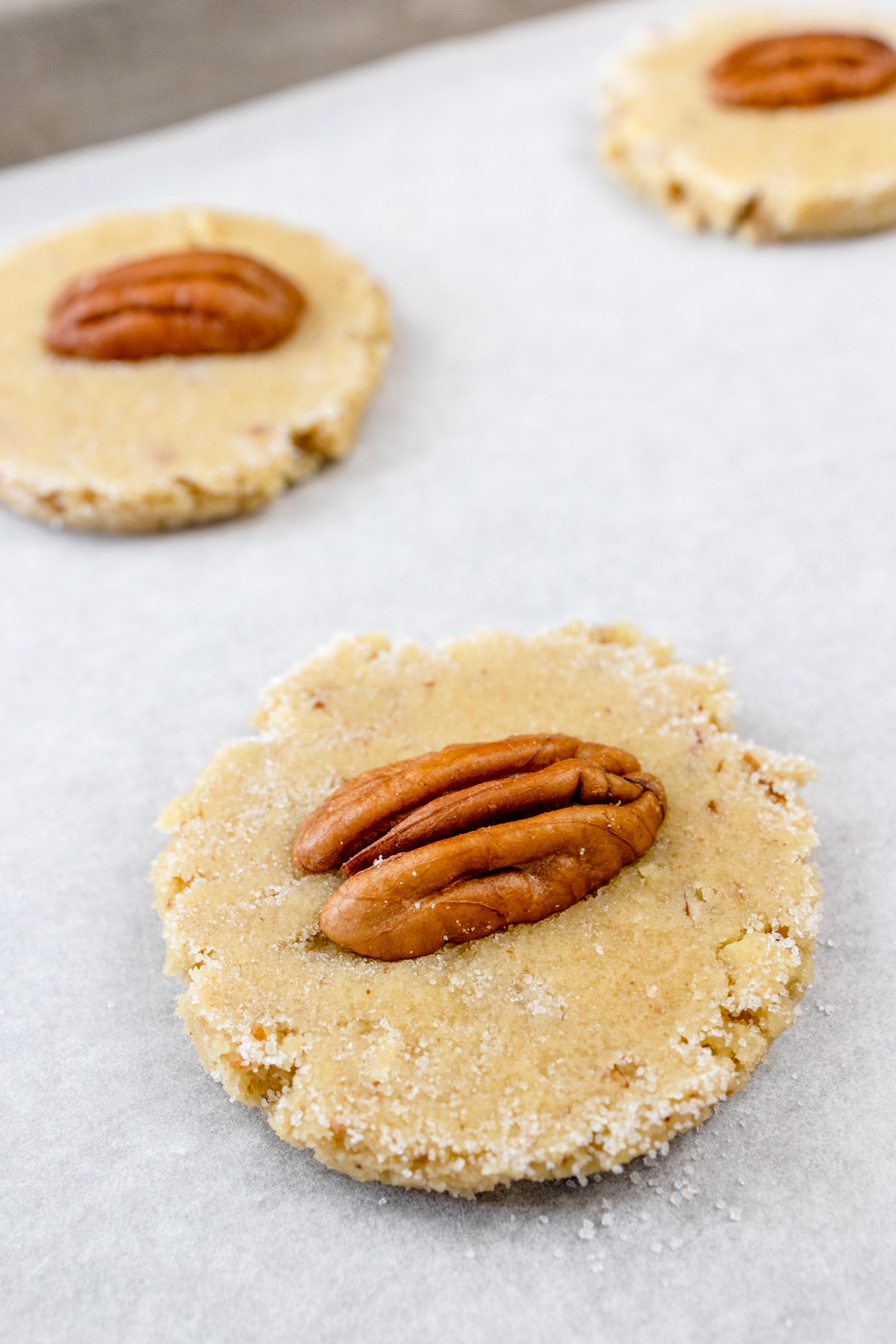 Close up of unbaked Pecan sandies cookies on parchment paper on a baking tray.